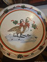 Front of round tin tray showing geese, ribbon and holly design