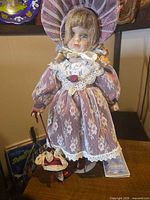 Full view of porcelain doll in mauve dress on stand with parasol and tag