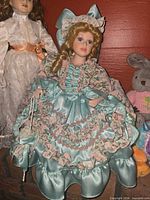 Full view of doll seated, showing dress, bonnet, pouch