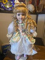 Front view of porcelain doll on stand showing dress, hair, shoes