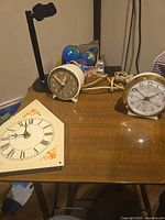 Two tabletop alarm clocks and clock face panel on table