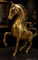 Front three-quarter view of brass rearing horse sculpture showing musculature, mane, and raised foreleg.