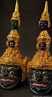 Front view of both guardian mask sculptures highlighting colors and gilt crowns