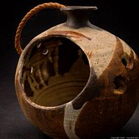 Front view showing spherical vessel, large cut-out opening, rope handle, glaze colors