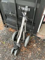 Full view of folded Evolution 3-wheel golf push cart leaning against container
