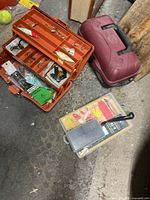 Orange tackle box open showing lures and gear beside maroon box and clear organizer