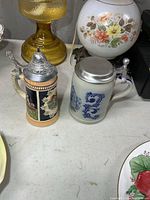 Both stoneware steins side by side showing overall design and lids