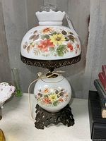 Front view showing floral milk glass shade, base, metal foot, chimney