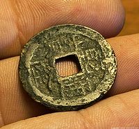 Front of bronze cash coin showing square hole and Chinese characters