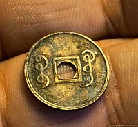 Close-up of both sides showing square hole and stylised characters, illustrating size and wear.