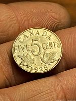 Reverse of 1928 Canada 5 cent coin showing denomination, maple leaves, date