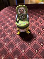 Front view of chair-shaped ceramic trinket box showing painted floral details and hinge