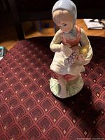 Front view of porcelain figurine showing girl, basket of fruit and color details