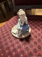Front view of porcelain figurine showing girl, cat, book, stool, round base