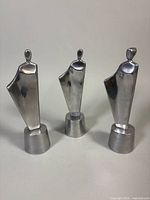 Three silver-tone metal statuettes standing upright