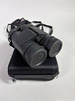 Binoculars resting on carrying case, showing objective lens caps and strap