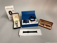 All three items laid out: Givenchy watch in box, Fitbit Charge 2 packaging and display tray, Apple Sport Band package