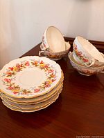 Stack of five floral rim plates beside four matching handled soup bowls