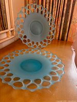 Two turquoise frosted glass plates showing openwork rims, one on stand, one flat on surface