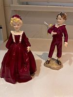Pair of burgundy-clad porcelain boy and girl figurines on countertop