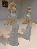 Two clear glass angel figurines standing side by side
