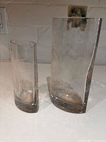 Two hammered-texture clear glass vases, one curved rectangular and one cylindrical