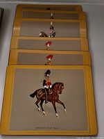 Stack of six identical wood-backed placemats showing British cavalry figure, yellow borders visible