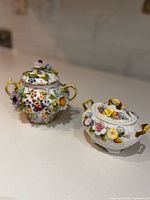 Two ornate porcelain sugar bowls with floral applique and lids