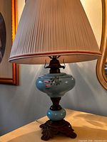 Full view of turquoise ceramic table lamp with floral design, metal base and pleated shade