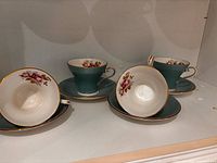 All four turquoise teacups with floral interiors and their matching saucers displayed