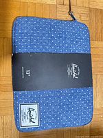 Front of blue polka dot Herschel laptop sleeve with logo patch and retail band