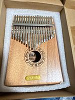 Top view of YAEL kalimba in foam insert showing brass badge and 17 tines