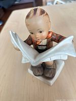 Front angled view of figurine showing boy reading newspaper and base