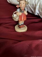front view of Hummel Goebel girl with basket figurine on burgundy surface