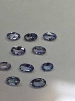 Ten oval cut Tanzanite gemstones displayed on grey background