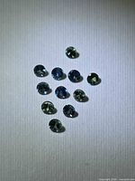 Group of 11 round blue and green sapphires on white background