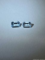 Pair of rectangular emerald-cut aquamarines on neutral background