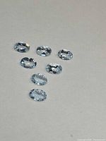Seven pale blue oval-cut gemstones on neutral background