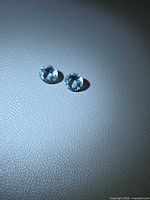 Pair of round faceted light blue aquamarine gemstones on textured surface