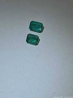 Two octagon-cut emeralds on light background