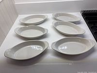 Six white oval handled dishes on countertop