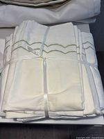 folded white duvet cover and shams tied with ribbon, showing green embroidered edge