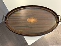 Top view of oval mahogany tray showing urn inlay and brass handles
