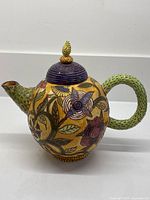 Side view of handmade ceramic teapot showing floral decoration, handle and spout