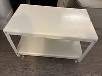 Front side view of white rolling cart with two shelves and wheels