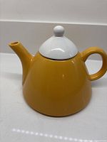 Side view mustard yellow ceramic teapot with white lid