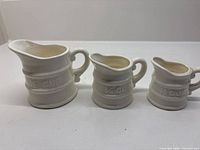 Front view of three white ceramic measuring cups showing embossed labels and handles