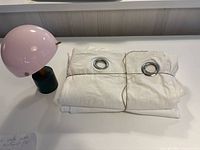 Folded white curtains with grommets and lamp visible