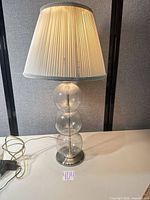 Full view of lamp showing glass base, metal accents, shade