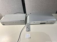 Both DVD/VHS combo players and remote control on tabletop